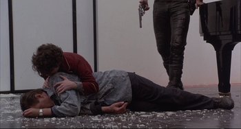 Movie still from “The Punisher” (1989), directed by Mark Goldblatt – A man laying on the ground while another man holds a gun; Medium shot, Over the shoulder angle