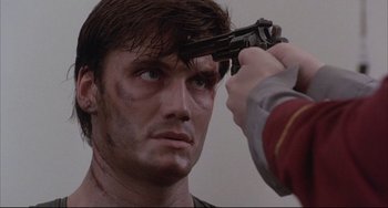 Movie still from “The Punisher” (1989), directed by Mark Goldblatt – A man is holding a gun up to his face; Close Up shot, Over the shoulder angle