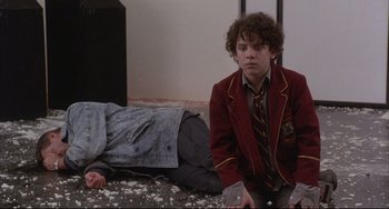 Movie still from “The Punisher” (1989), directed by Mark Goldblatt – A young man in a red jacket sitting on the ground next to another man; Medium shot, High angle