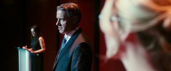 Movie still from “The Purge: Election Year” (2016), directed by James DeMonaco – A man wearing a suit and tie standing in front of a wall; Close Up shot, Over the shoulder angle