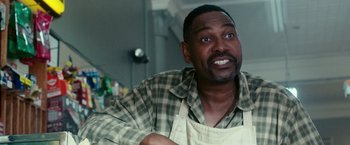 Movie still from “The Purge: Election Year” (2016), directed by James DeMonaco – A man in a plaid shirt and an apron is smiling for the camera; Close Up shot, Over the shoulder angle