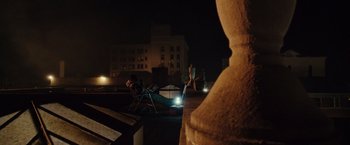 Movie still from “The Purge: Election Year” (2016), directed by James DeMonaco – A person sitting on a chair on top of a building at night; Wide shot, High angle