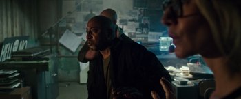 Movie still from “The Purge: Election Year” (2016), directed by James DeMonaco – A man standing in a room with other people; Medium shot, Over the shoulder angle