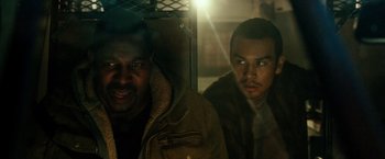 Movie still from “The Purge: Election Year” (2016), directed by James DeMonaco – Two men are sitting next to each other in the dark; Close Up shot, Over the shoulder angle