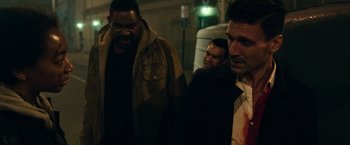 Movie still from “The Purge: Election Year” (2016), directed by James DeMonaco – A group of men standing next to each other on a street; Medium shot, Over the shoulder angle