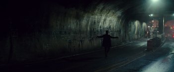 A person walking in a dark tunnel with graffiti on the wall