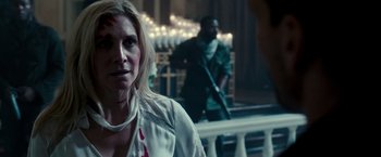 Movie still from “The Purge: Election Year” (2016), directed by James DeMonaco – A woman in white shirt holding a gun in front of a building; Close Up shot, Over the shoulder angle