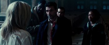 Movie still from “The Purge: Election Year” (2016), directed by James DeMonaco – A man in a trench coat and tie standing next to two other men; Medium shot, Over the shoulder angle