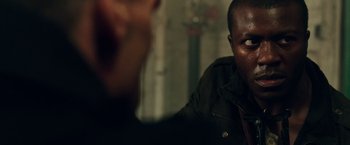 Movie still from “The Purge: Election Year” (2016), directed by James DeMonaco – A man sitting in front of another man in front of a wall; Close Up shot, Over the shoulder angle