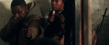 Movie still from “The Purge: Election Year” (2016), directed by James DeMonaco – A man holding a gun while standing next to a wall; Medium shot, Over the shoulder angle