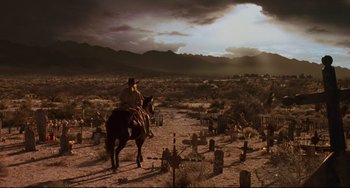 Movie still from “The Quick and the Dead” (1995), directed by Sam Raimi – A man riding a horse through a graveyard; Extreme Wide shot, Low angle