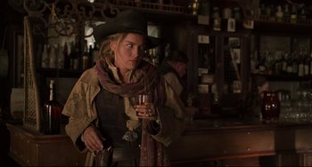 Movie still from “The Quick and the Dead” (1995), directed by Sam Raimi – A woman holding a glass of wine while wearing a cowboy hat; Medium shot, Over the shoulder angle