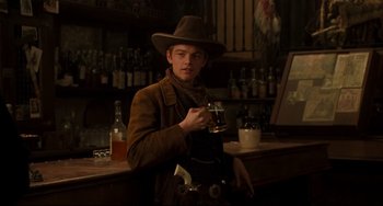 Movie still from “The Quick and the Dead” (1995), directed by Sam Raimi – A man holding a glass of beer standing in front of a bar; Medium shot, Over the shoulder angle