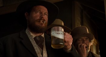 Movie still from “The Quick and the Dead” (1995), directed by Sam Raimi – A man with a beard holding a beer in his hand; Close Up shot, Low angle