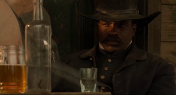 Movie still from “The Quick and the Dead” (1995), directed by Sam Raimi – A man in a hat and a jacket is looking at a glass; Close Up shot, Low angle