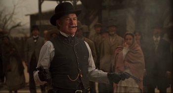 Movie still from “The Quick and the Dead” (1995), directed by Sam Raimi – An old man in a black hat holding a gun in front of a group of people; Medium shot, Low angle