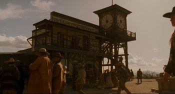Movie still from “The Quick and the Dead” (1995), directed by Sam Raimi – A group of people walking in front of a building with a clock tower; Extreme Wide shot, Low angle
