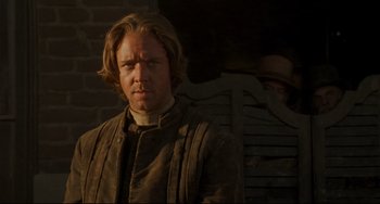 Movie still from “The Quick and the Dead” (1995), directed by Sam Raimi – A man with long blonde hair wearing a brown jacket; Close Up shot, Over the shoulder angle