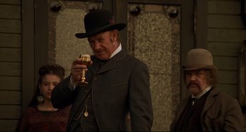 Movie still from “The Quick and the Dead” (1995), directed by Sam Raimi – An old man in a suit and a black hat holding a wine glass; Medium shot, Low angle