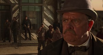 Movie still from “The Quick and the Dead” (1995), directed by Sam Raimi – A group of people standing around a man in a hat; Close Up shot, Over the shoulder angle