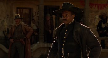 Movie still from “The Quick and the Dead” (1995), directed by Sam Raimi – A man wearing a cowboy hat standing next to another man; Medium shot, Over the shoulder angle