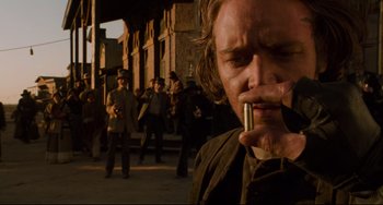 Movie still from “The Quick and the Dead” (1995), directed by Sam Raimi – A man smoking a cigarette in front of a group of people; Close Up shot, Low angle
