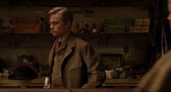 Movie still from “The Quick and the Dead” (1995), directed by Sam Raimi – A man in a suit and tie standing next to a counter; Medium shot, Low angle