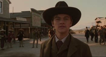 Movie still from “The Quick and the Dead” (1995), directed by Sam Raimi – A man in a suit and hat standing in front of a building; Medium shot, Low angle