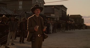 Movie still from “The Quick and the Dead” (1995), directed by Sam Raimi – A man in a suit and hat holding a pair of binoculars in front of a group of people; Medium shot, Low angle