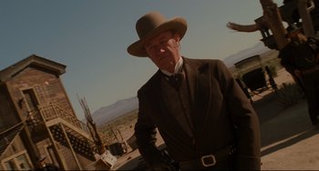 Movie still from “The Quick and the Dead” (1995), directed by Sam Raimi – An older man in a suit and hat standing in front of a windmill; Medium shot, Low angle