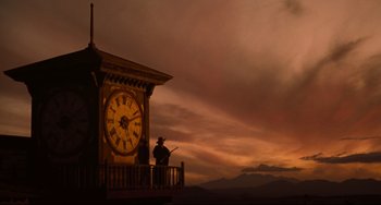 Movie still from “The Quick and the Dead” (1995), directed by Sam Raimi – A man standing in front of a large clock; Extreme Wide shot, Low angle