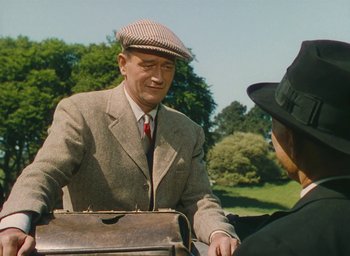 Movie still from “The Quiet Man” (1952), directed by John Ford – An older man in a suit and hat holding a briefcase; Medium shot, Over the shoulder angle
