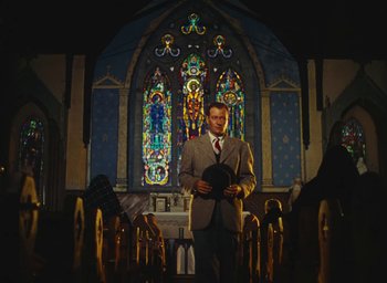 Movie still from “The Quiet Man” (1952), directed by John Ford – A man standing in front of a stained glass window; Wide shot, Low angle