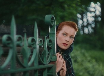 Movie still from “The Quiet Man” (1952), directed by John Ford – A woman leaning on a green fence looking over her shoulder; Medium shot, High angle