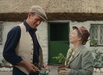 Movie still from “The Quiet Man” (1952), directed by John Ford – An older man and woman holding plants outside a house; Medium shot, Low angle