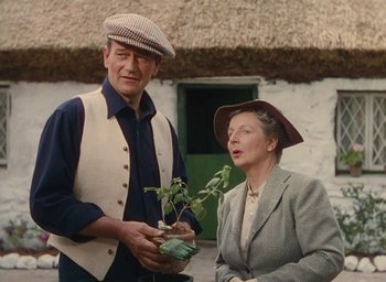 Movie still from “The Quiet Man” (1952), directed by John Ford – An older man and woman standing next to each other holding a plant; Medium shot, Low angle