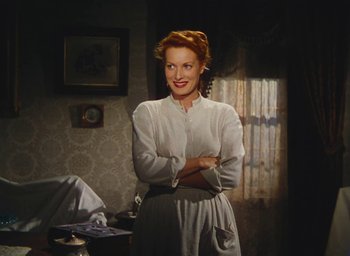 Movie still from “The Quiet Man” (1952), directed by John Ford – A woman standing in a room with her arms crossed; Medium shot, High angle
