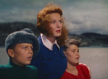 Movie still from “The Quiet Man” (1952), directed by John Ford – A woman and two children standing next to each other in front of a body of water; Medium shot, Low angle