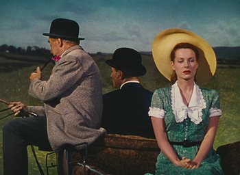 Movie still from “The Quiet Man” (1952), directed by John Ford – A man and a woman sitting on a bench in a field; Medium shot, Low angle