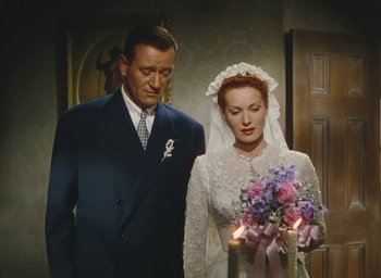 Movie still from “The Quiet Man” (1952), directed by John Ford – A man and a woman standing next to each other holding candles; Medium shot, High angle