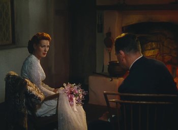 Movie still from “The Quiet Man” (1952), directed by John Ford – A man and a woman sitting at a table holding a bouquet of flowers; Medium shot, High angle
