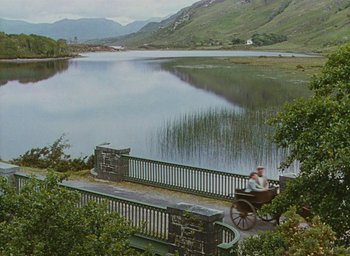 Movie still from “The Quiet Man” (1952), directed by John Ford – A man sitting on top of a horse drawn carriage on top of a bridge over a lake; Extreme Wide shot, High angle