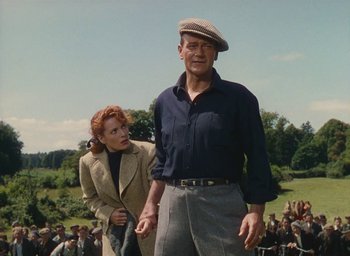 Movie still from “The Quiet Man” (1952), directed by John Ford – A man and a woman are standing in front of a group of people; Medium shot, Low angle