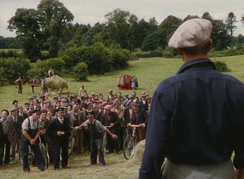 Movie still from “The Quiet Man” (1952), directed by John Ford – A group of people standing in front of a man holding a bicycle; Extreme Wide shot, High angle