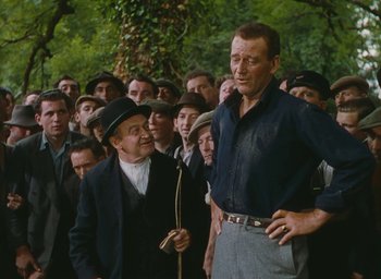 Movie still from “The Quiet Man” (1952), directed by John Ford – A group of men standing next to each other in front of trees; Medium shot, Over the shoulder angle