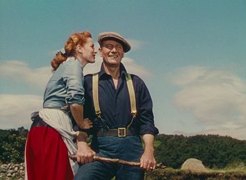 Movie still from “The Quiet Man” (1952), directed by John Ford – An older man and a young woman standing next to each other holding a stick; Medium shot, Low angle