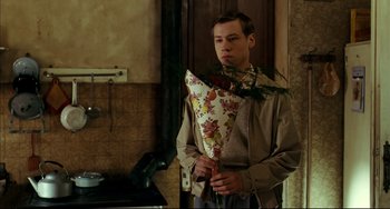 Movie still from “The Reader” (2008), directed by Stephen Daldry – A man holding a bouquet of flowers in a kitchen; Medium shot, Over the shoulder angle