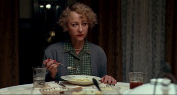 Movie still from “The Reader” (2008), directed by Stephen Daldry – A woman sitting at a dinner table with a plate of food; Medium shot, Over the shoulder angle