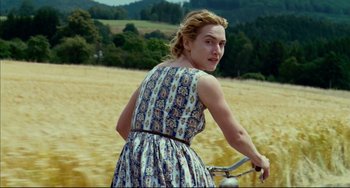 Movie still from “The Reader” (2008), directed by Stephen Daldry – A woman riding a bike through a field; Medium shot, High angle