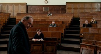 Movie still from “The Reader” (2008), directed by Stephen Daldry – Three people sitting in a lecture hall with a clock in the background; Wide shot, High angle